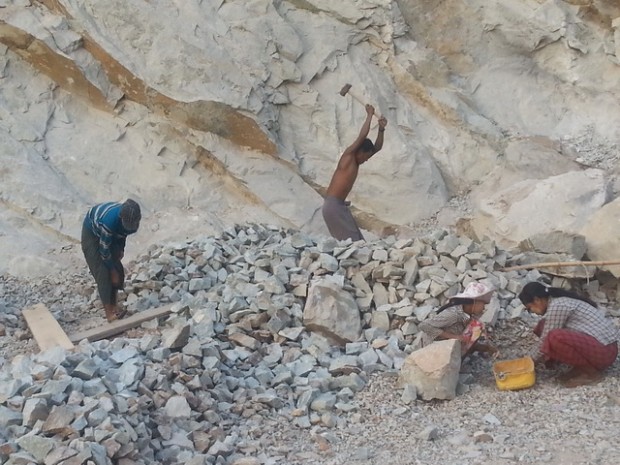 คนงานก่อสร้างถนนเชื่อมไทย-พม่า กำลังทุบหินให้กลายเป็นก้อนเล็กๆ ด้วยค้อน และคัดแยกขนาดหินด้วยมือ เพื่อนำมาสร้างถนน